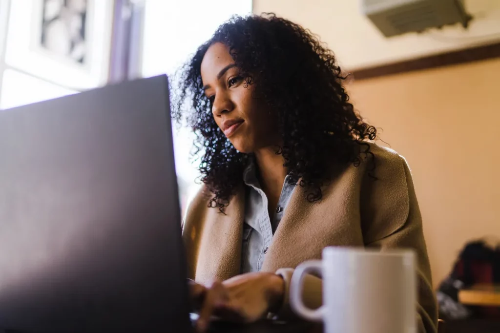 Woman working on laptop in cozy room with a mug nearby.
