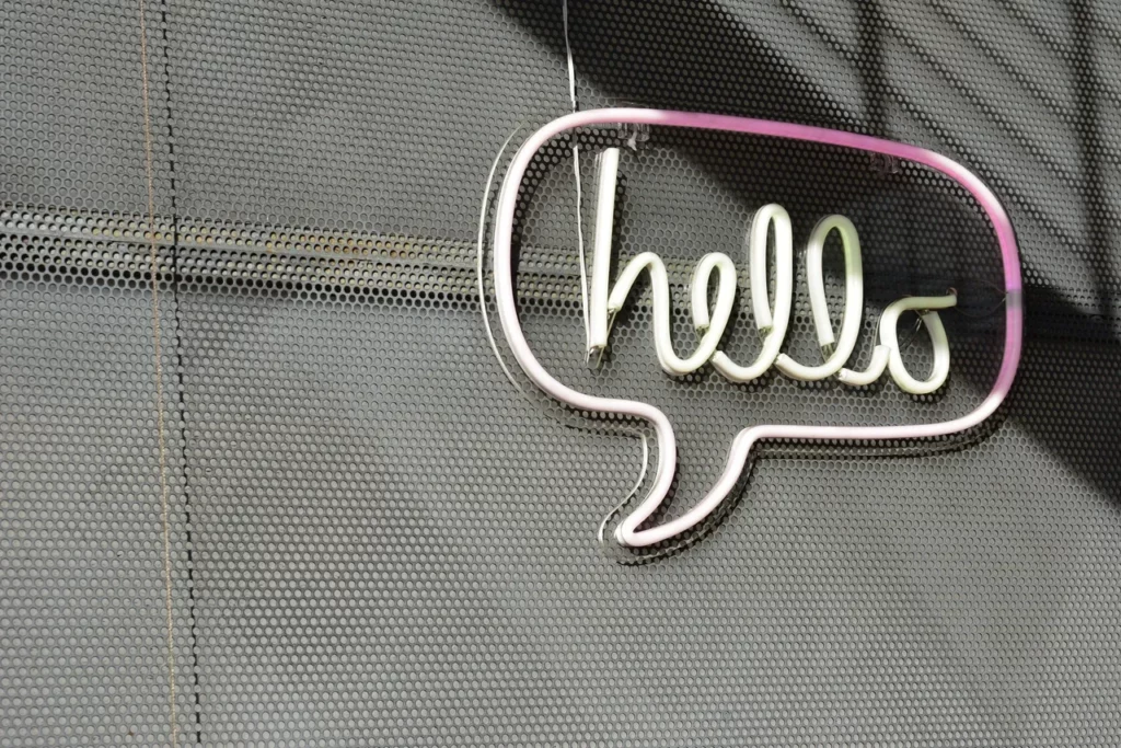 Neon sign displaying Hello in speech bubble on perforated wall.