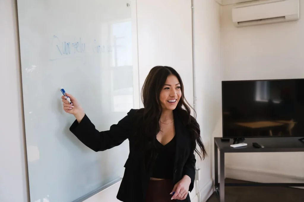 Smiling woman teaching at whiteboard.
