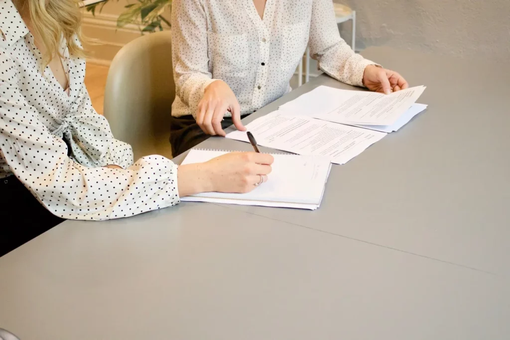 Hands writing and pointing at papers on a table in an office.