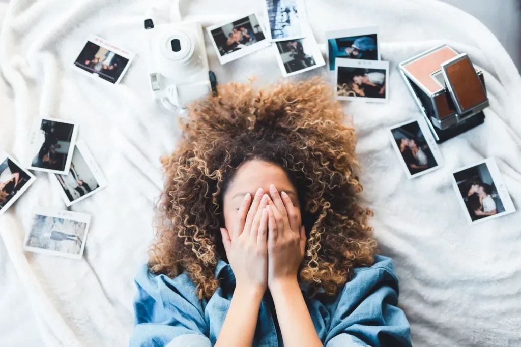 Person covering face, surrounded by photos on a white blanket.